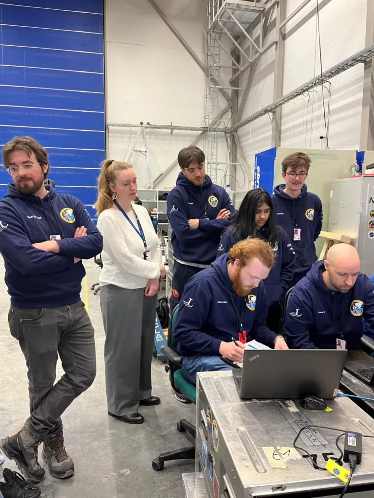 Seven young space engineers in front of a laptop preparing for a space mission