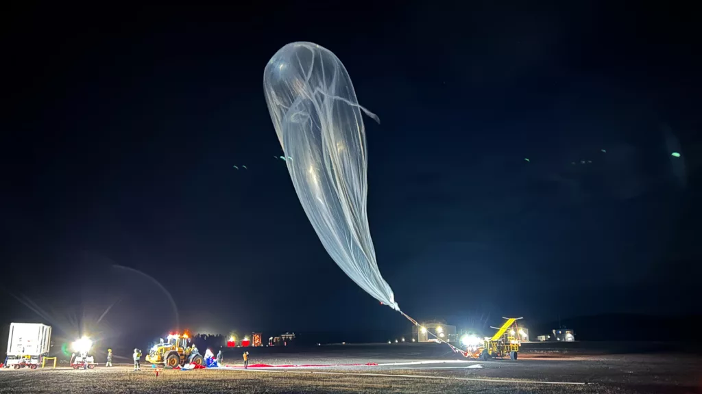 A giant balloon rises in the pitch black sky.