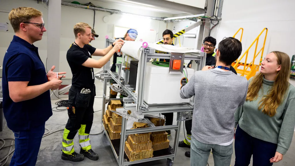 Six persons working on a balloon payload standing on a wheel trolley