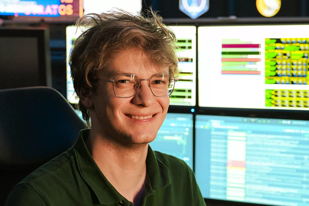 Ilja smiling, sitting next to screens at GSOC.