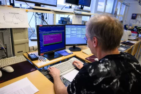 A man sitting in front of an old computer with two separate monitors.